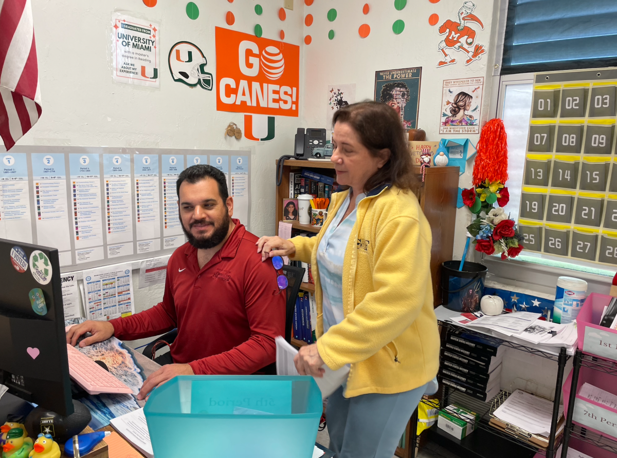 Aiding in technical issues, Mr. Jorge Lopez repairs Ms. Marion Chase's computer, allowing her and her students to complete their schoolwork without impediments. 